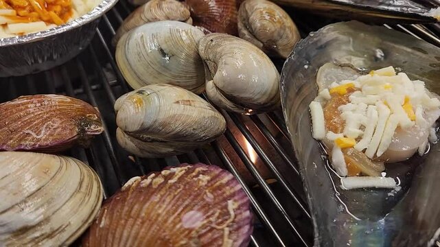 한국 영종도 월미도 해수욕장 바닷가 음식점의 석쇠에 올려 놓은 가리비 키조개 동죽 조개들이 뜨거운 불에 구워지면서 입을 벌리는 