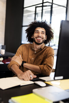 Smiling man in office working on computer, feeling accomplished and motivated