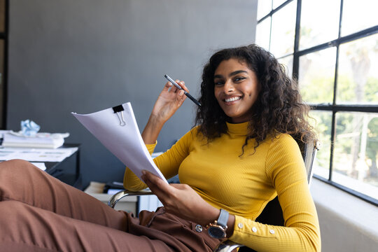 Confident woman reviewing documents and smiling at office desk
