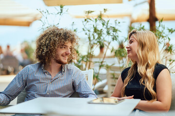 Business Pair Discussing Work During a Break in a Caffee Garden, Using a Tablet and Papers