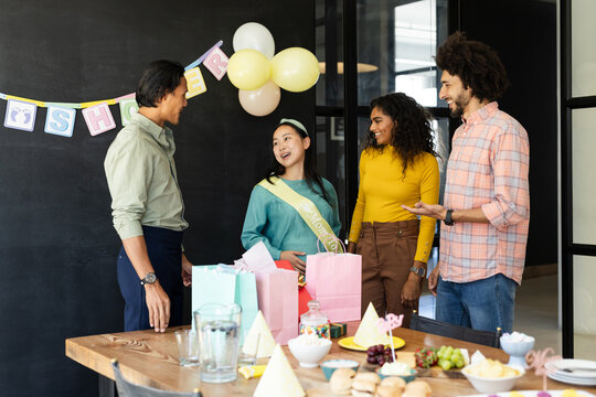 Diverse colleagues celebrating baby shower with gifts and decorations in office setting