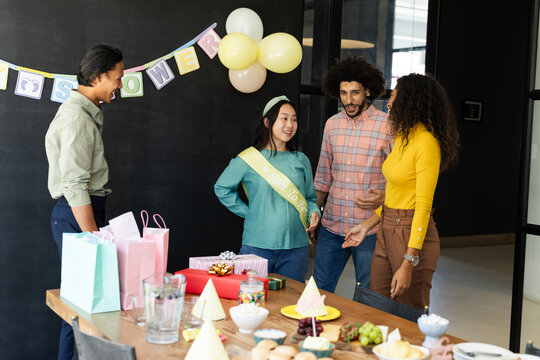 Diverse colleagues celebrating baby shower with gifts and decorations in office setting