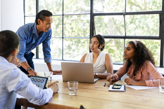 Business diverse team collaborating at table with laptops and tablets in modern office