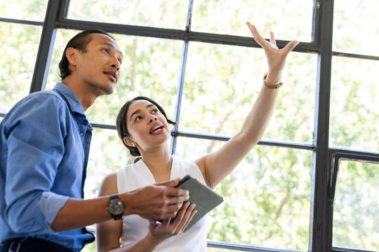 Diverse colleagues discussing project details while using tablet near large office window
