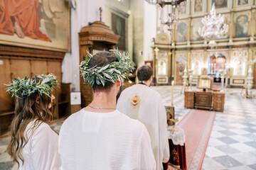 Montenegro, Kotor - July 07, 2024: Bride and groom in wreaths stand behind the priest conducting the marriage ceremony. Back view