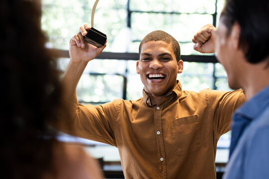 man celebrating success holding trophy in office with diverse colleagues - Powered by Adobe