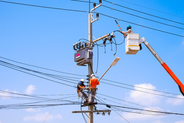 Electricians group with crane truck are installing electrical equipment on electric power pole...