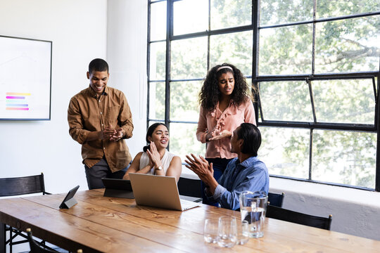 Diverse team collaborating around table with laptops in modern office setting
