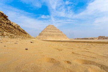 A ground-level view of the Step Pyramid of Zoser, showcasing its grandeur against the vast desert...