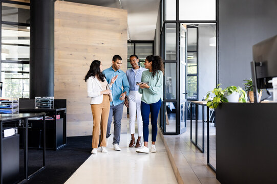 Diverse business team walking in modern office, discussing project on tablet