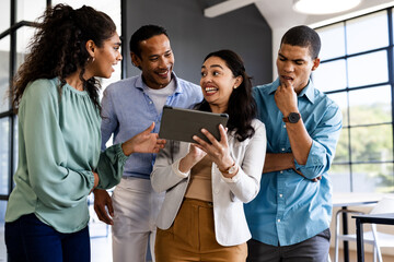 Diverse business team discussing project while looking at tablet in modern office