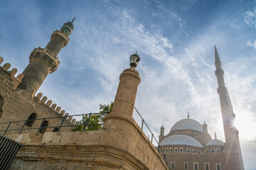 A low-angle view of the Mohamed Ali Mosque, showcasing its minaret and domes against a blue sky. A...