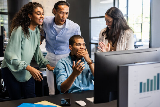 Collaborating on project, diverse team discussing ideas around computer in office