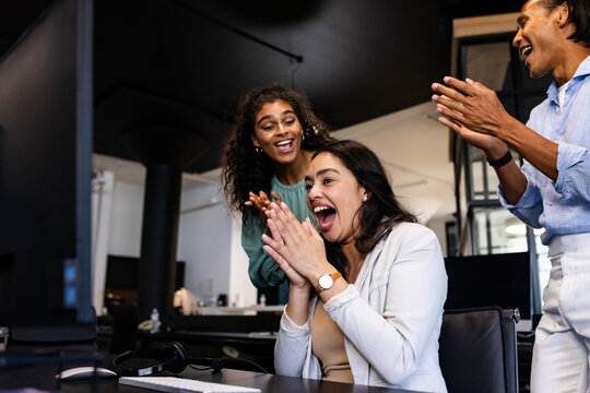 Diverse diverse colleagues celebrating success at office, clapping and smiling at computer