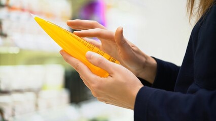 A customer reading label with ingredients examines composition in cosmetics store, choosing...