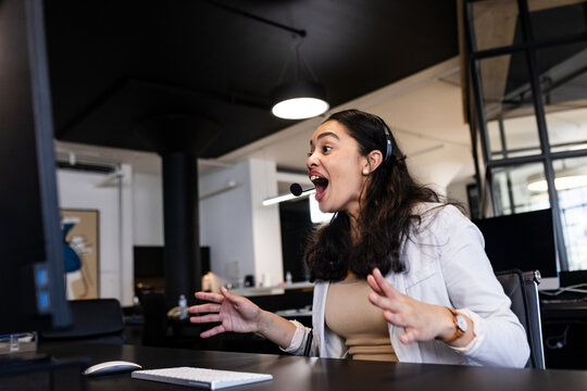 Excited woman in office using headset, engaging in lively video conference