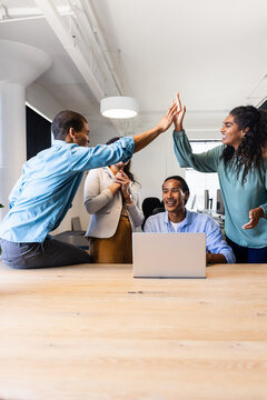 Diverse business team celebrating success with high fives in modern office, copy space