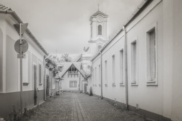A timeless street view of Szentendre, Hungary, featuring cobblestone paths and classic architecture. The baroque church tower in the background enhances the historic, nostalgic atmosphere