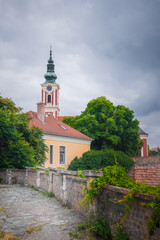 The Belgrade Cathedral of Serbian Orthodox Church in Szentendre, Hungary, with its striking baroque tower and pastel hues. A charming historical site surrounded by lush greenery and old stone paths