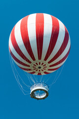 A striking red-and-white striped tethered balloon rising against a vibrant blue sky in Budapest’s City Park (Városliget). The perspective from below enhances the sense of height and adventure