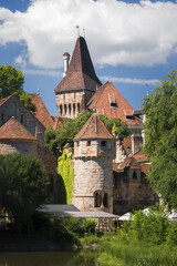 Vajdahunyad Castle in Budapest’s City Park blends medieval, Renaissance, and Baroque styles. Its towers and stone walls rise amid lush greenery, framed by ancient trees under a vivid blue sky