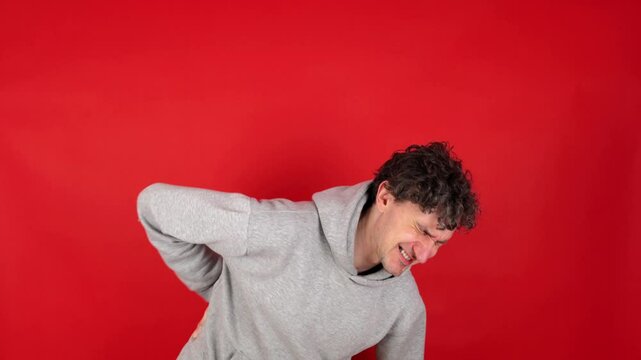 man suffers from back pain, sports injury, muscle spasm. who has lower back pain side problems after training, jogging. back flank ache problem after exercise. Isolated red background, studio shot.