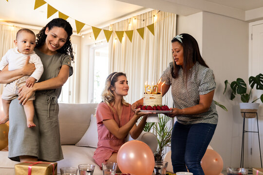 Birthday, diverse female friends with baby enjoying cake and decorations at home