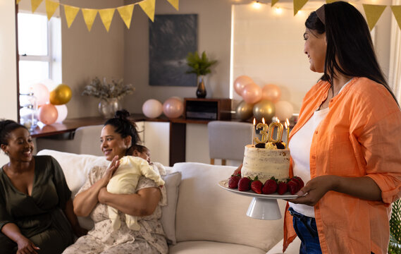 Birthday, woman bringing cake to diverse female friends on cozy living room sofa, at home