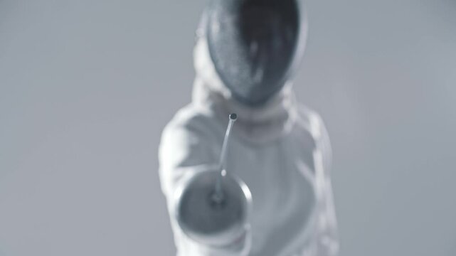 Fencing - young woman fencer in white suit aiming in the camera with a rapier