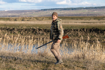 Mature hunter man holding a shotgun and walking through a field