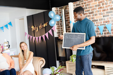Man holding chalkboard at Baby shower, guests smiling and enjoying celebration