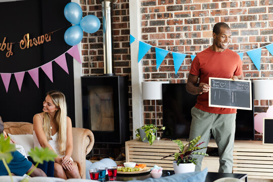Man holding chalkboard at Baby shower, guests smiling and enjoying celebration