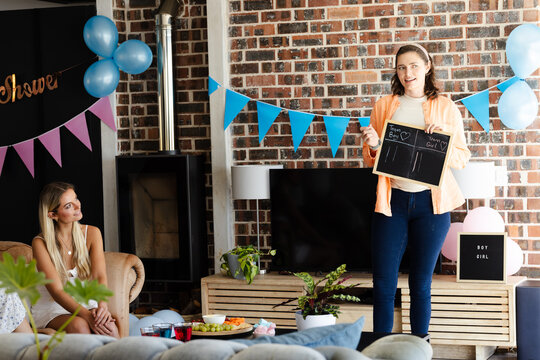 Woman holding chalkboard at Baby shower, diverse friends celebrating with decorations