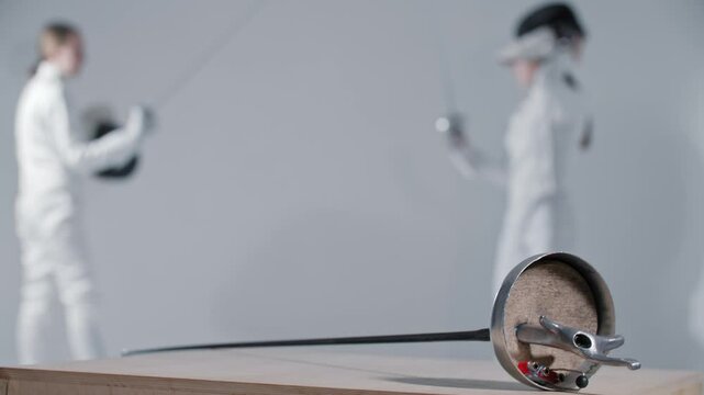 Fencing - two young women fencers having a training fight - a rapier on the foreground