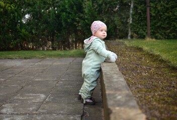 Obraz premium Baby girl in mint soft shell bodysuit is playing in a back yard in spring. Toddler girl walking on tiles footpath outside.