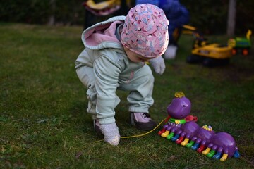 Baby girl in mint soft shell bodysuit is playing with toy centipede in a back yard in spring sunny...