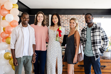 Housewarming, Group of diverse friends celebrating at home with balloons and gift, smiling together