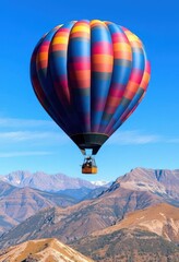 Obraz premium Vibrant hot air balloon ascends over majestic mountains, clear blue sky, freedom, panorama