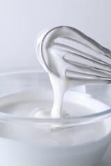Whisk and bowl with whipped cream on white background, closeup