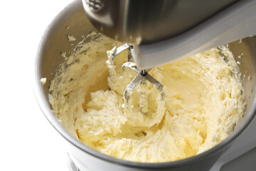 Mixing whipped cream in bowl with stand mixer on white table, closeup