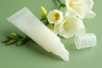 Lip balm and freesia flowers on light green background, closeup