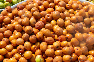 A pile of dried jujube fruits with a rich brown-red hue, their wrinkled texture showing they’ve been dried. Fresh green jujubes peek in the background, adding contrast to this market display.