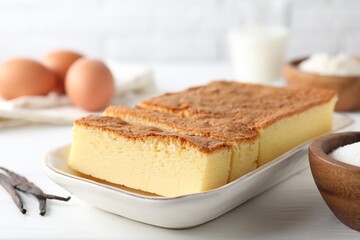 Tasty Japanese Castella sponge cake and ingredients on white table, closeup