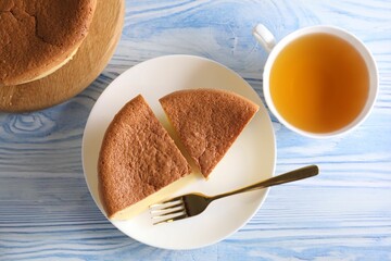 Tasty Japanese Castella sponge cake, tea and fork on light blue wooden table, flat lay