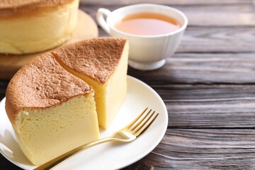 Pieces of tasty Japanese Castella sponge cake, tea, gypsophila flowers and fork on wooden table, closeup. Space for text