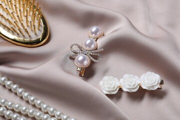 Beautiful hair clips, pearl necklace and brush on beige fabric, closeup