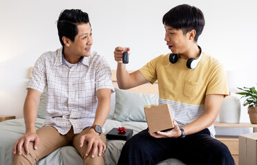 Asian father and son exchanging car keys and gift box, smiling at home