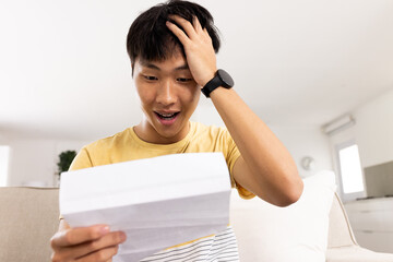 Surprised young man reading letter at home, expressing excitement and disbelief