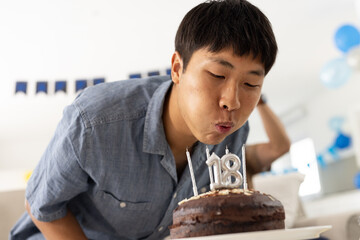 Asian man blowing out candles on birthday cake, celebrating 18th birthday at home