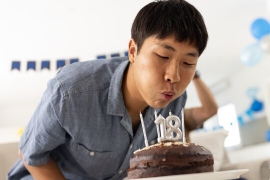 Asian man blowing out candles on birthday cake, celebrating 18th birthday at home